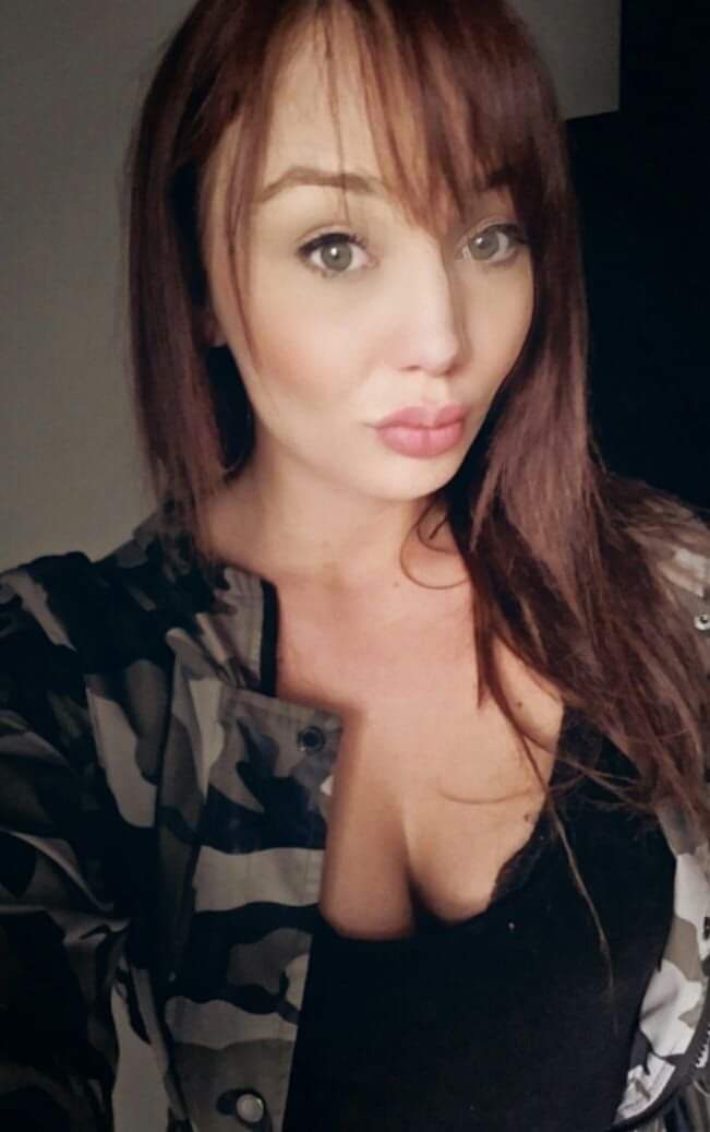 Selfie of Alex wearing camo print jacket, showing her cleavage and pouting,